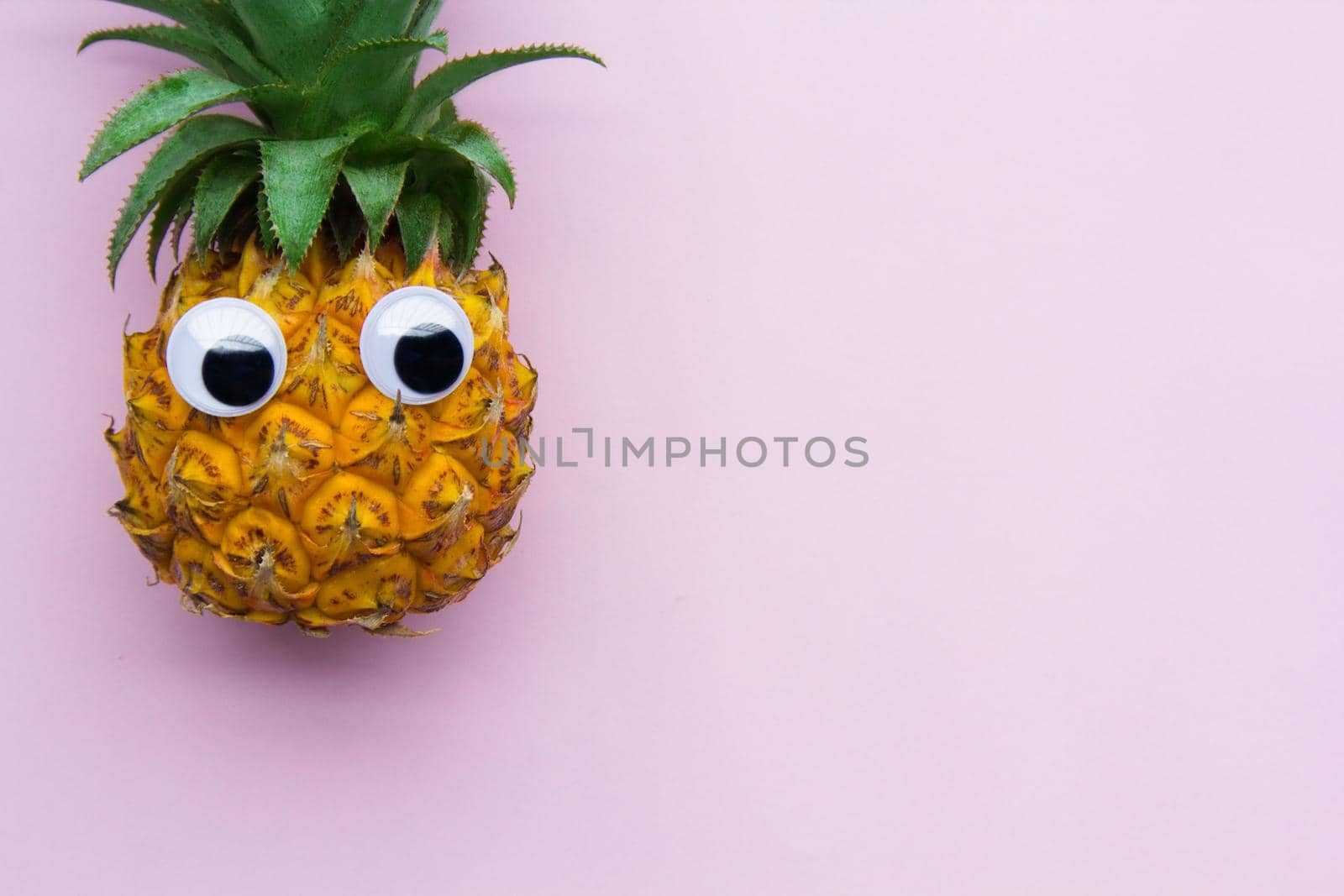 Fresh funny pineapple with googly eyes on pink background, enough place for text. .