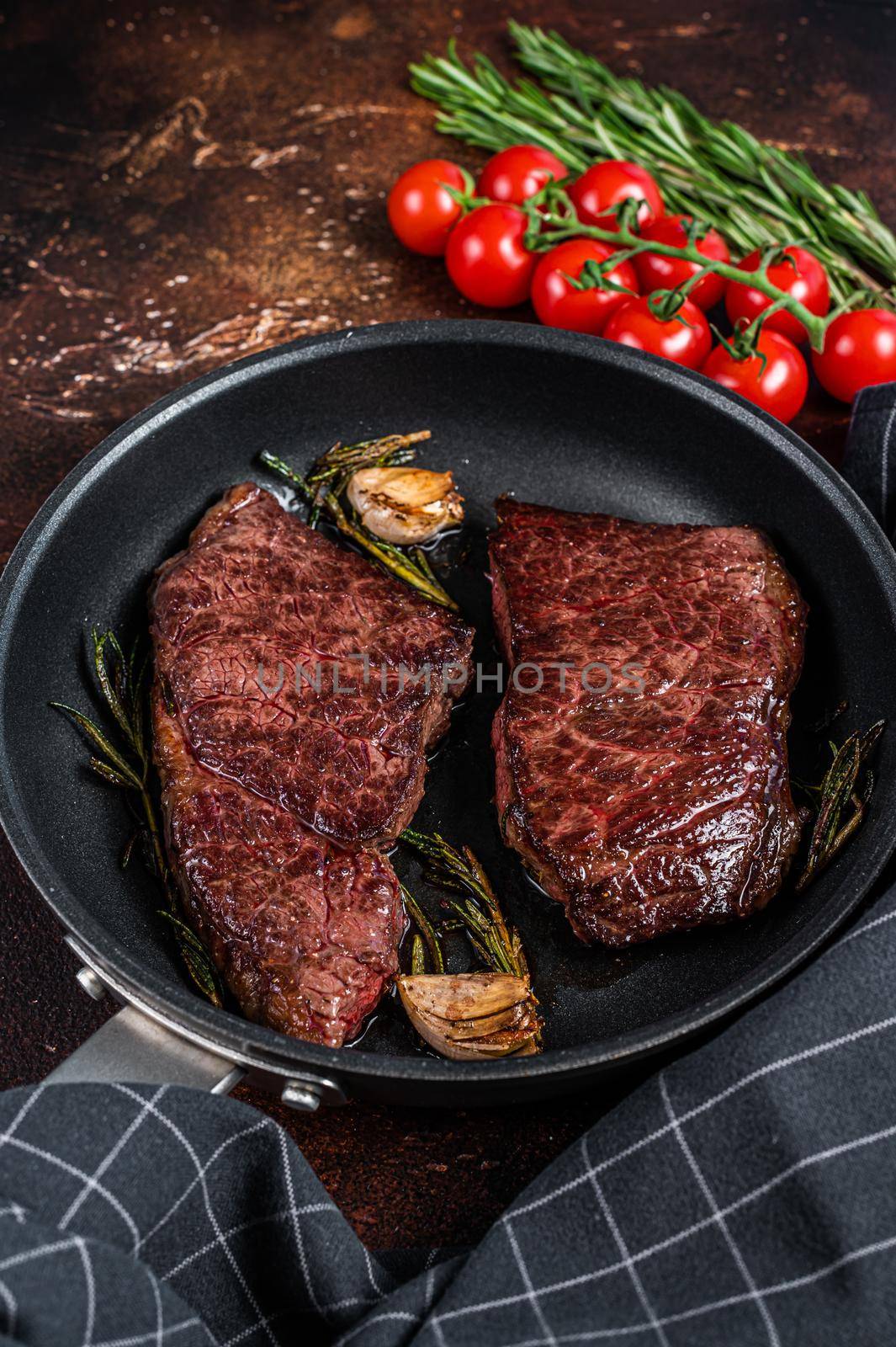 Grilled denver beef meat steak in a pan with rosemary. Dark background. Top view.