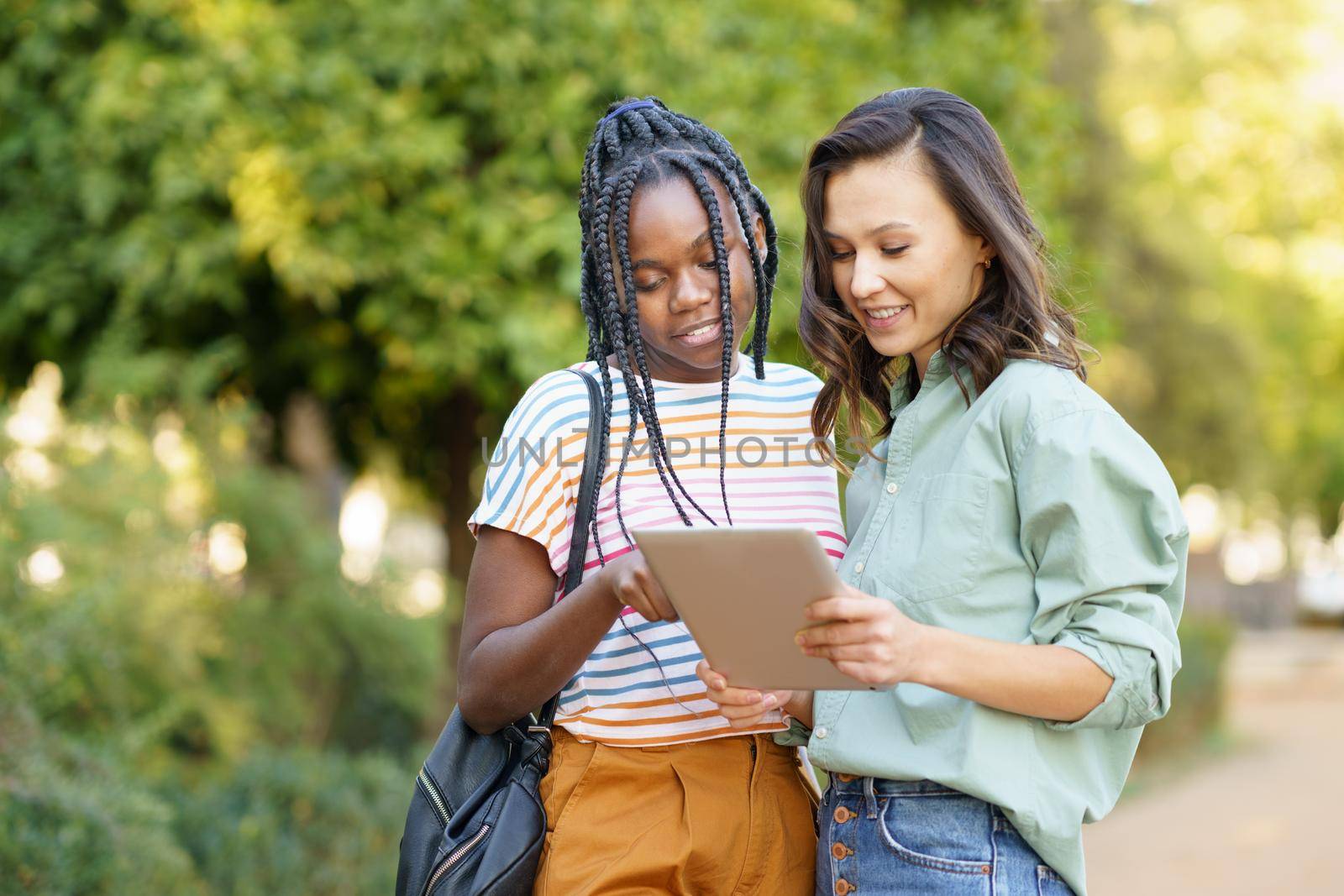 Two multiethnic women consulting something on a digital tablet outdoors.