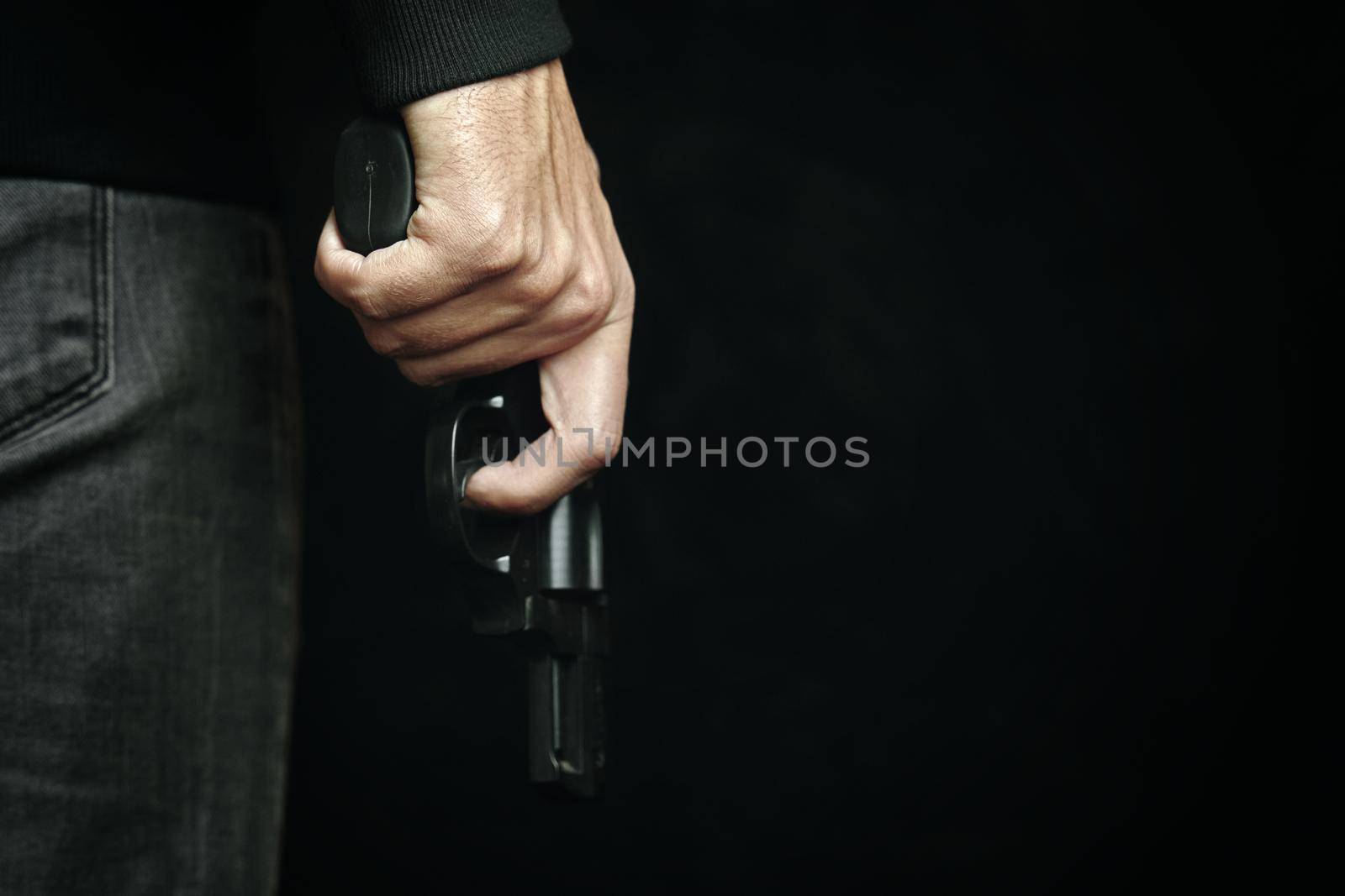 Criminal with revolver in his hand. Firearm for defense or attack. Killer on black background. Man in dark clothing is holding gun.