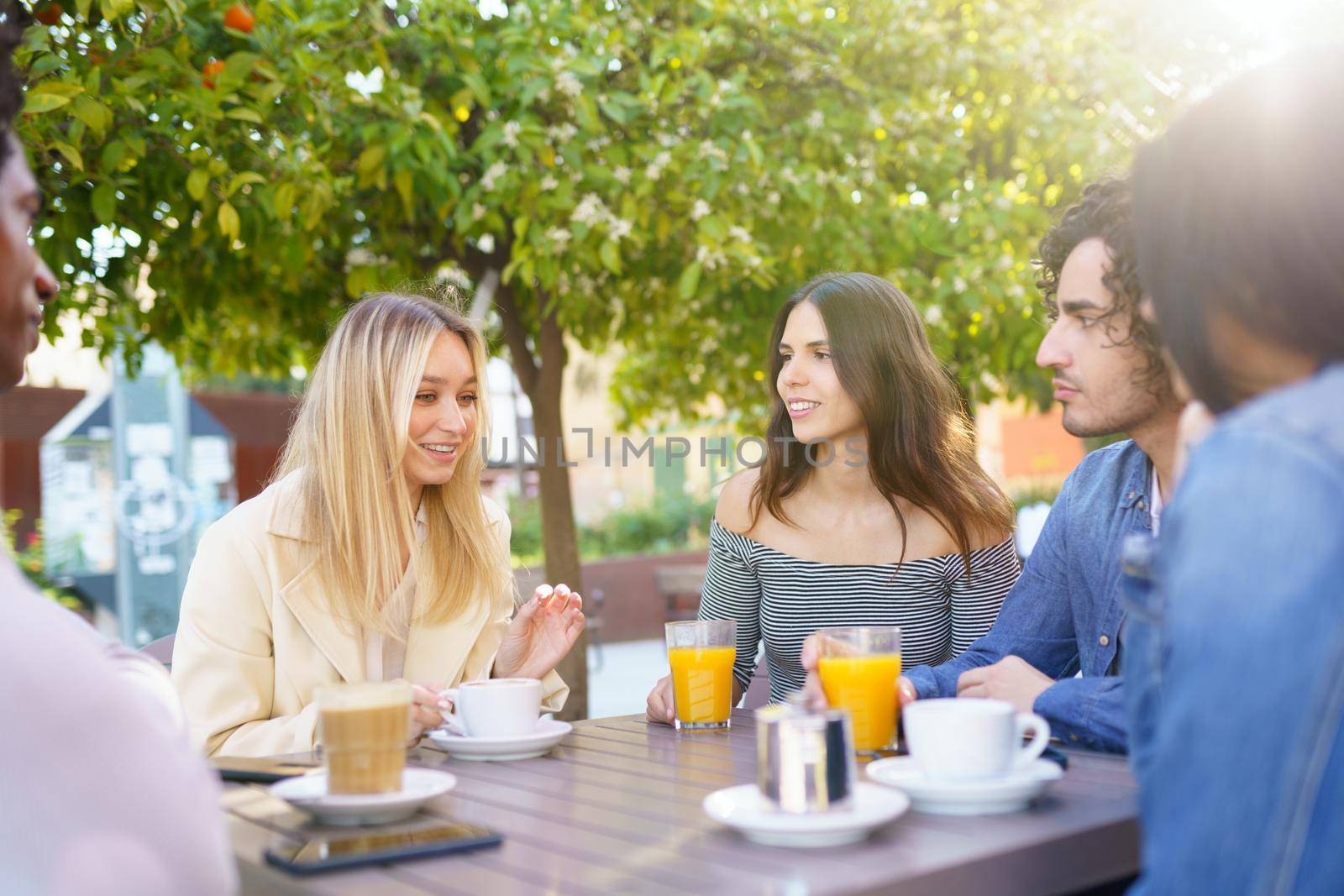 Multi-ethnic group of students having a drink on the terrace of a street bar. Young people having fun together