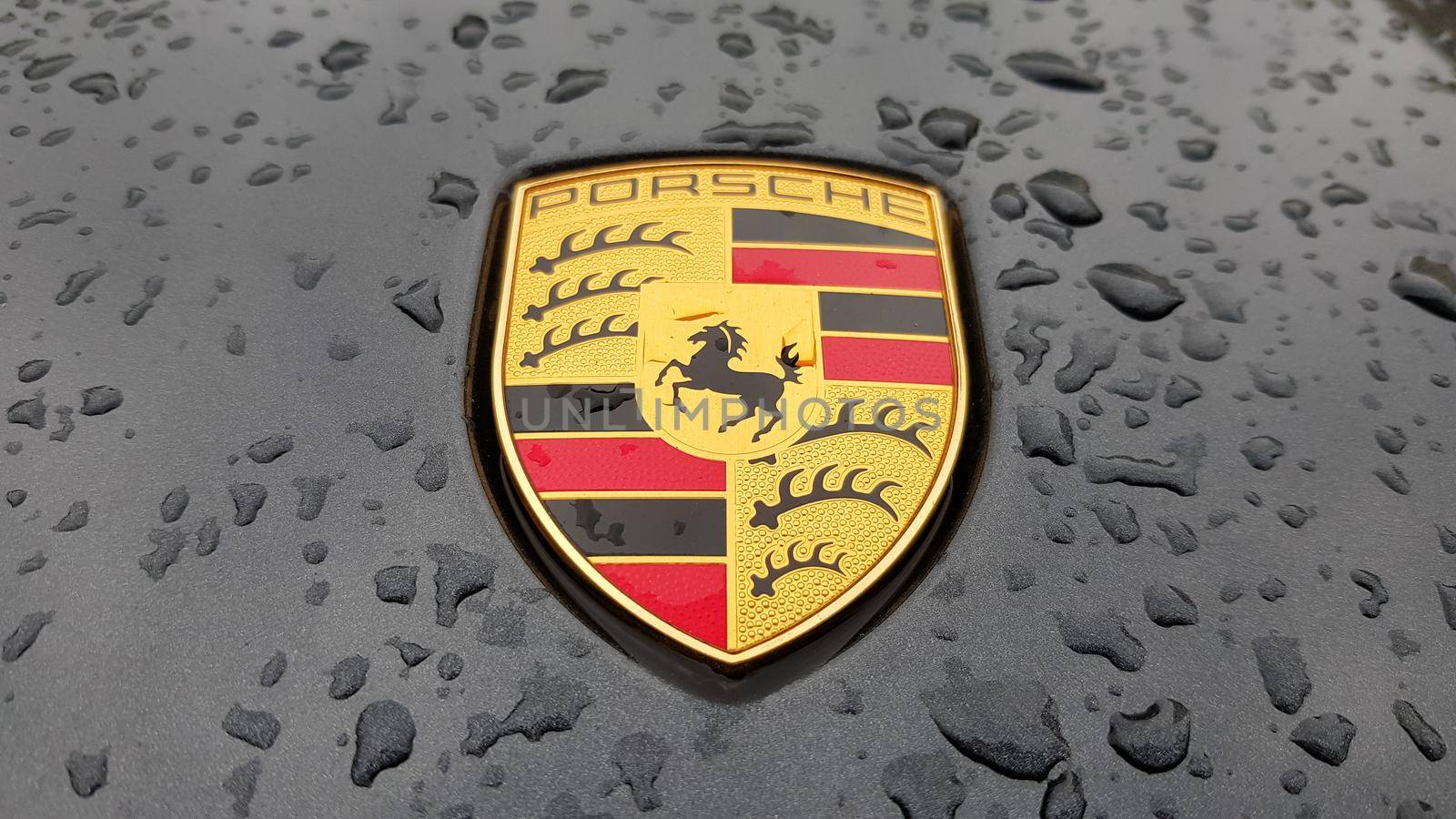 Ukraine, Kiev - March 27, 2020: Porsche logo close up on a black car with raindrops. Hood emblem of a sports car. copy space, editorial photography. German car exhibition on the street