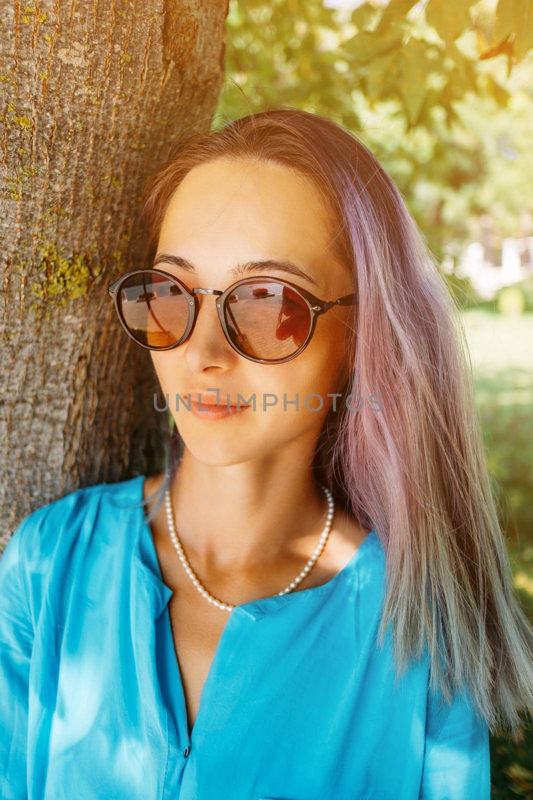 Portrait of stylish beautiful young woman wearing in sunglasses near a tree in summer park.