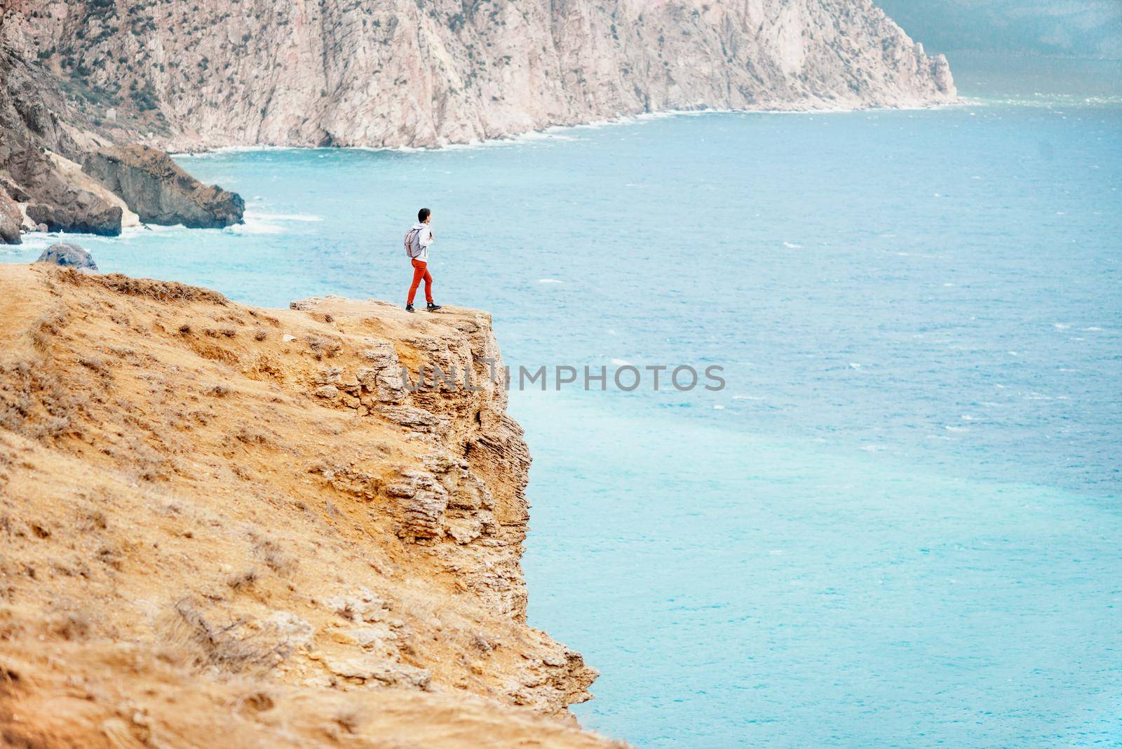 Backpacker traveler young woman standing on edge of cliff over sea.