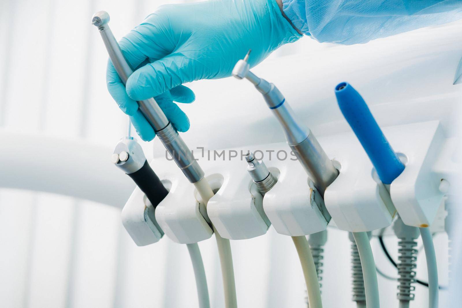 a dentist wearing gloves in the dental office holds a tool before working by Lobachad