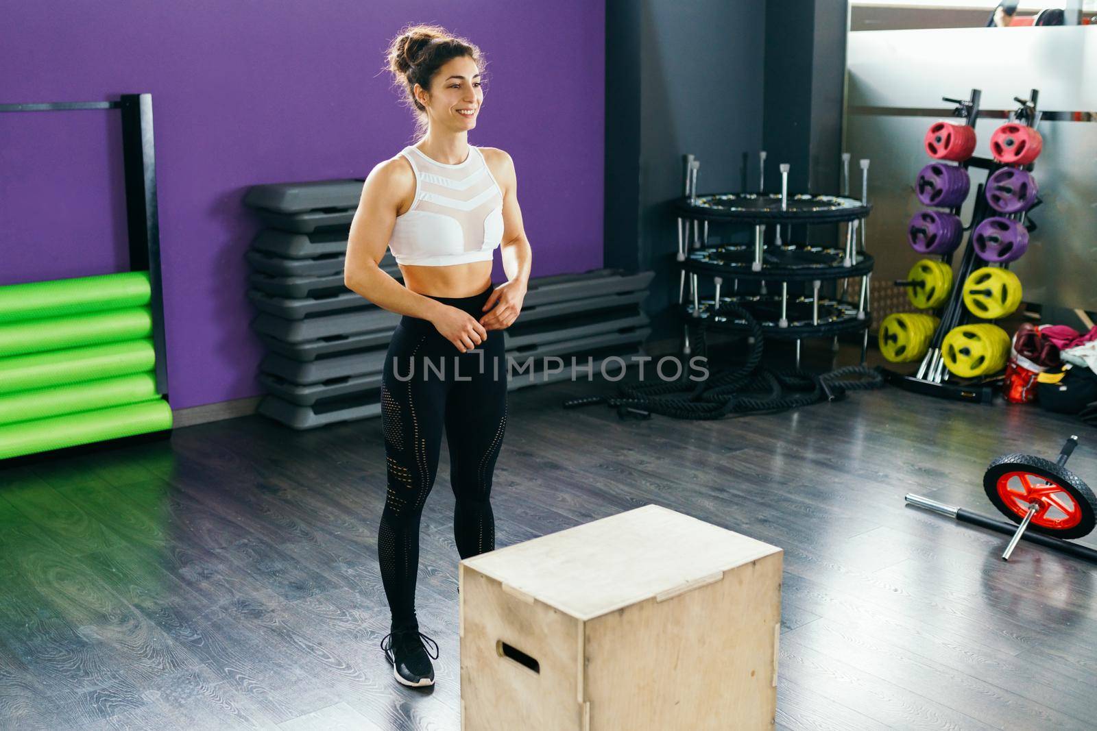 Fitness woman jumping onto a box as part of exercise routine. Caucasian female doing box jump workout at gym.