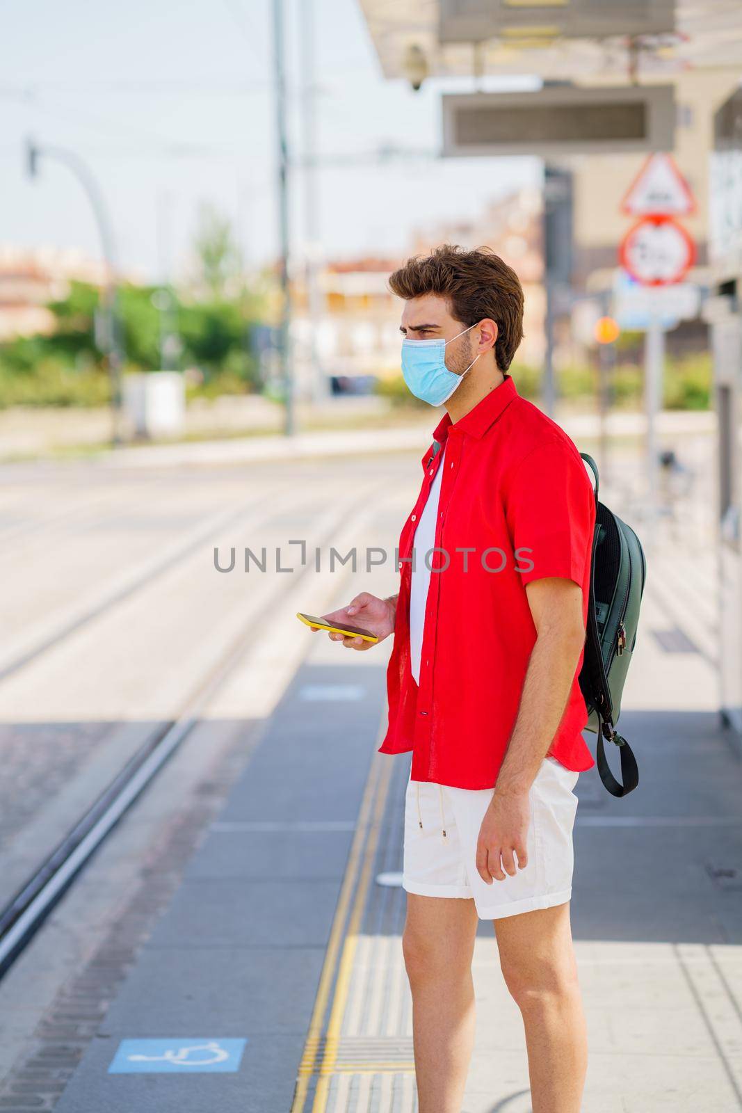 Student male wearing a surgical mask while waiting for a train at an outside station