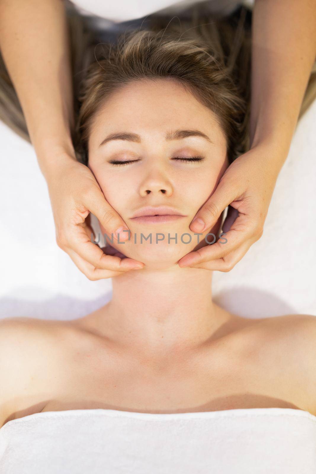 Young woman receiving a head massage in a spa center. Female patient is receiving treatment by professional therapist.