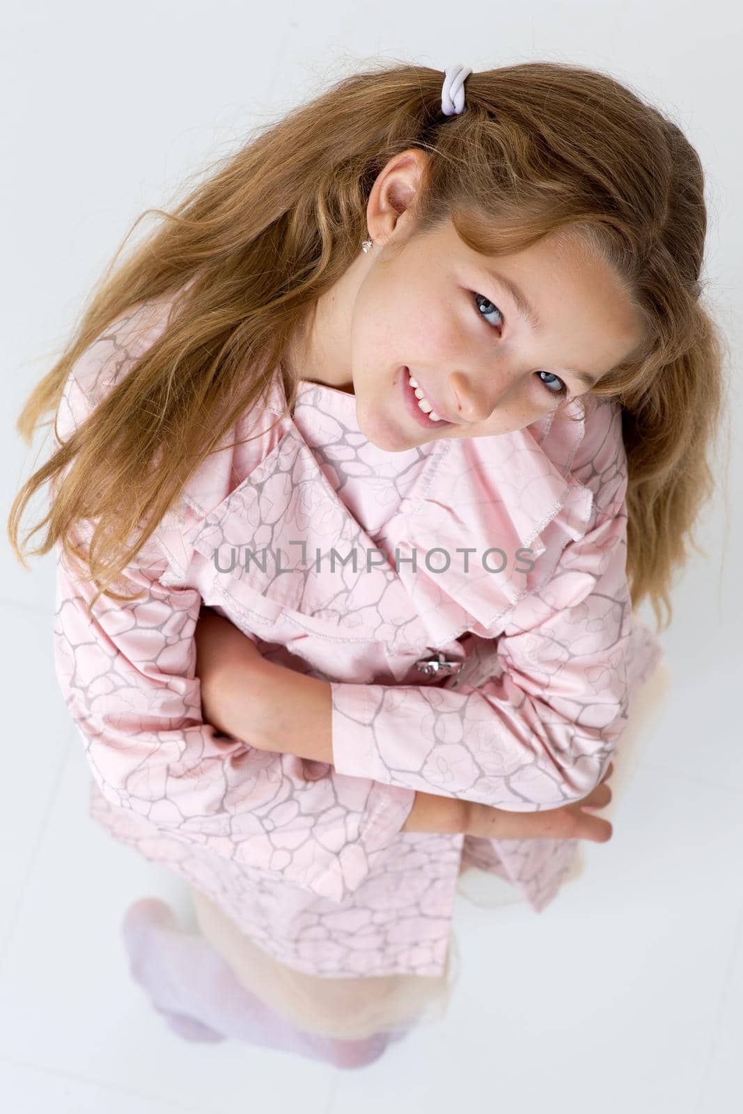 Above view of pretty girl in raincoat standing and looking up. Happy blonde preteen girl posing in studio against white background. Happy childhood concept