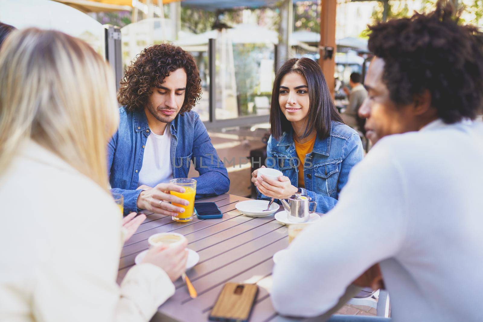 Multi-ethnic group of students having a drink on the terrace of a street bar. Young people having fun together