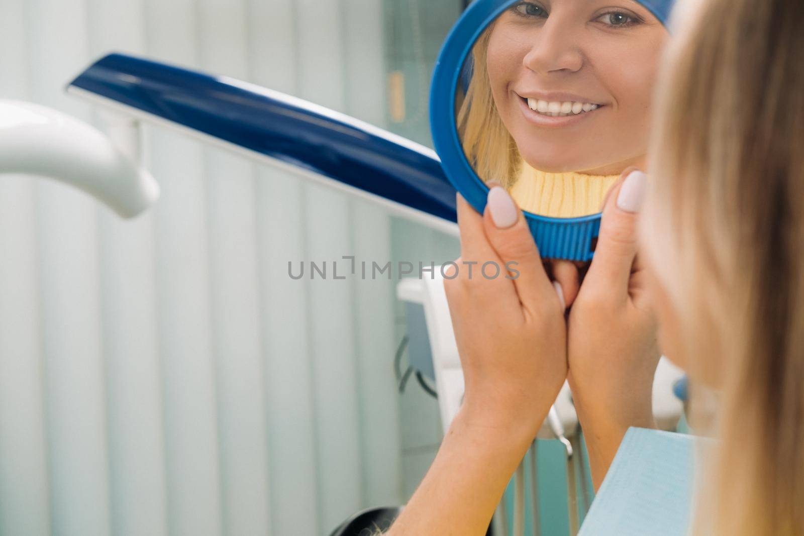 The girl smiles and looks in the mirror in dentistry.