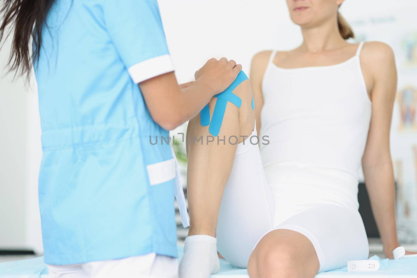 Close-up of female patient bend knee, woman athlete with kinesiotape, blue muscle tape. Professional physiotherapist help to recovery after accident. Rehabilitation concept