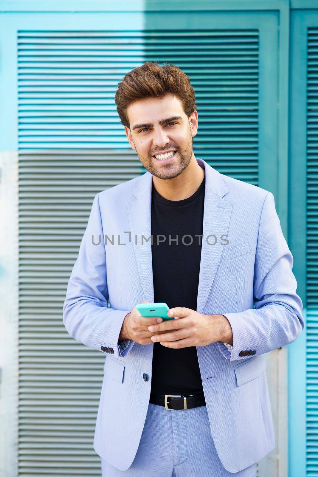 Young businessman wearing blue suit using a smartphone in urban background. Man with formal clothes in the street.