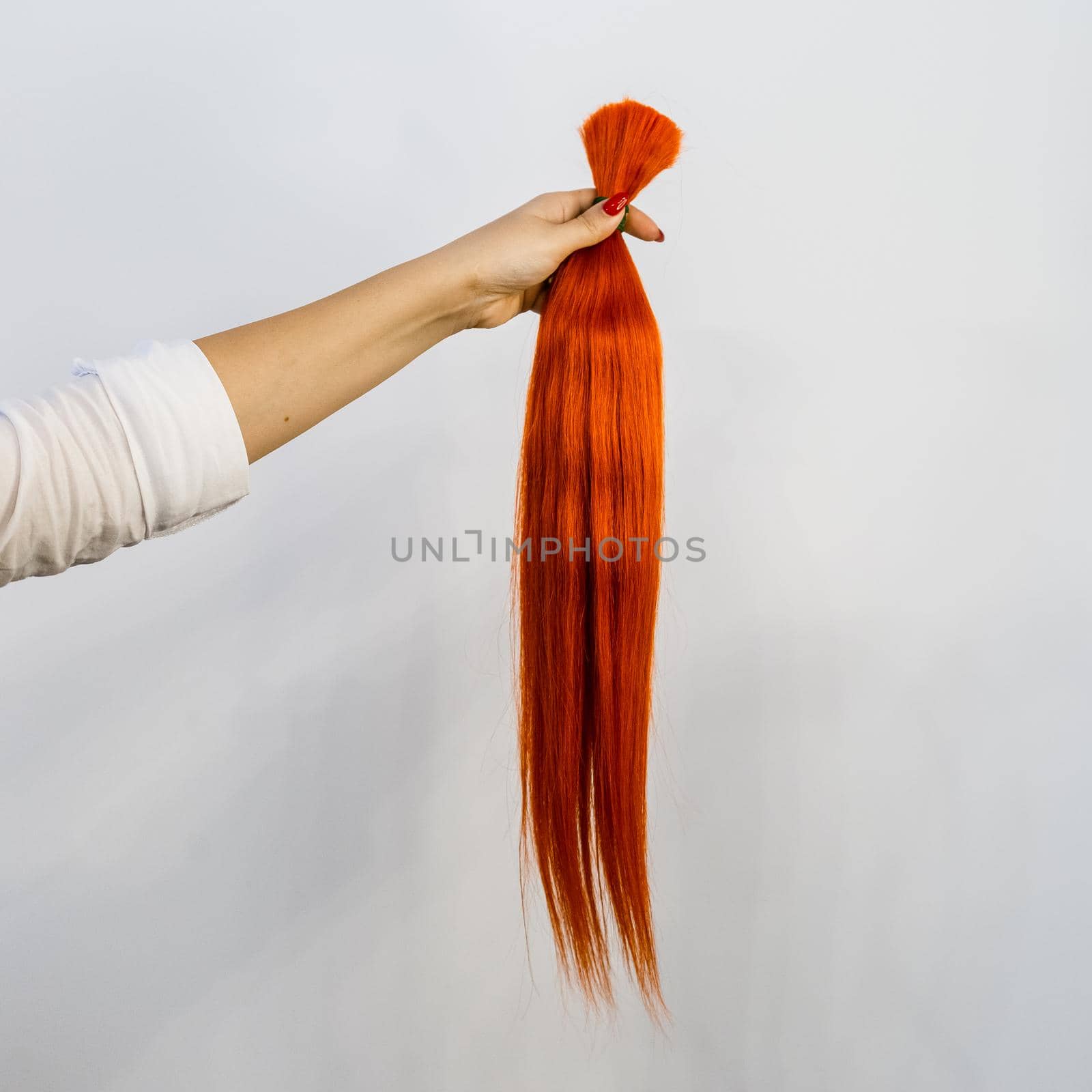 Famale hand holding a bundle of red natural remy human hair extensions over white background