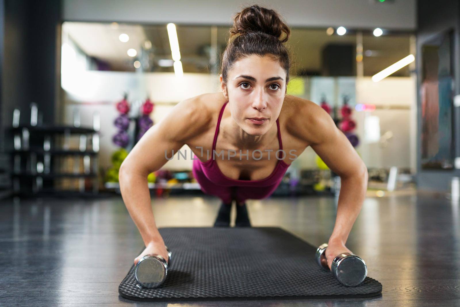 Woman doing push-ups exercise with dumbbell in a fitness workout by javiindy