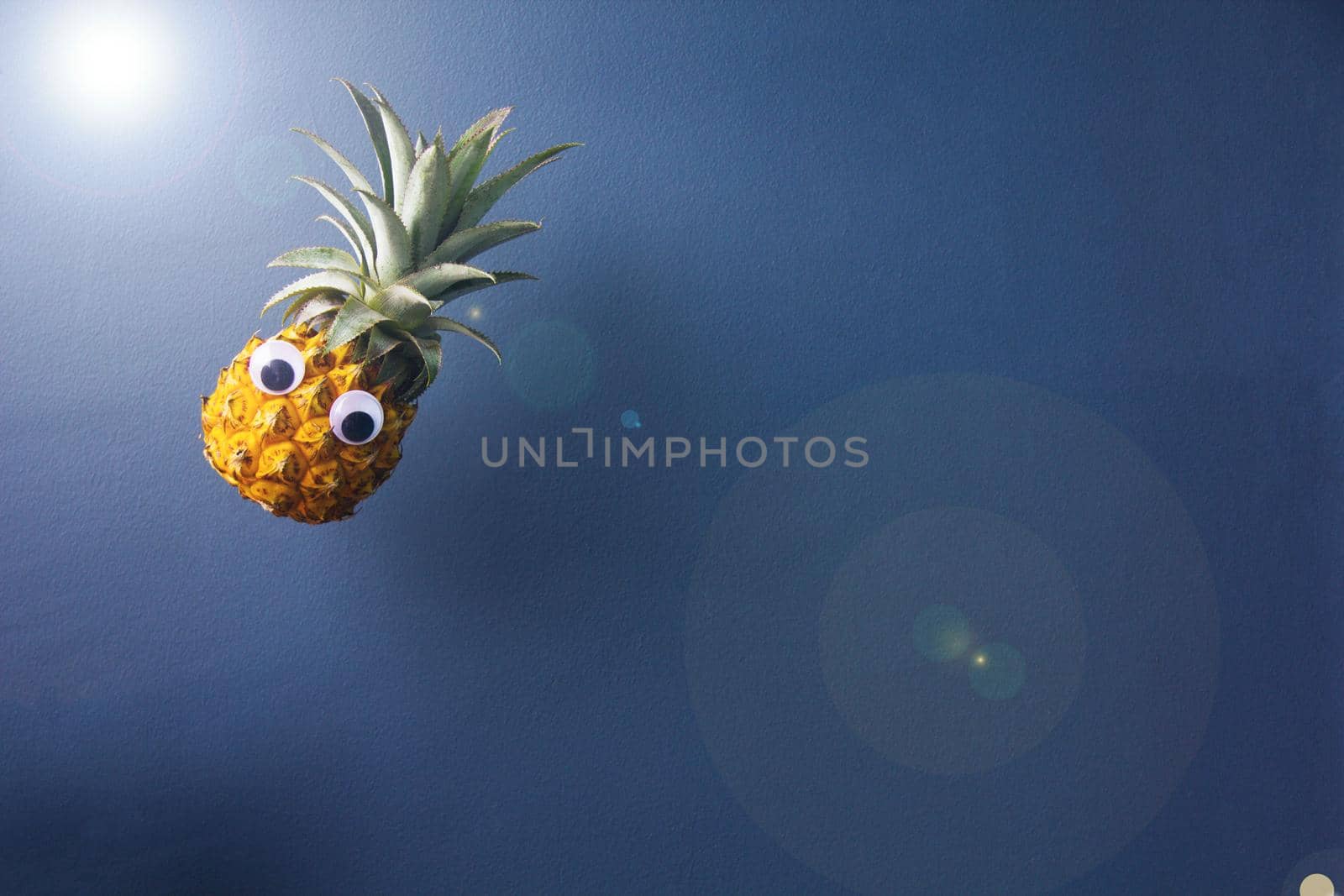 Fresh pineapple with googly eyes looks like flying, hang on air on blue background, enough place for text. Good concept for magic.