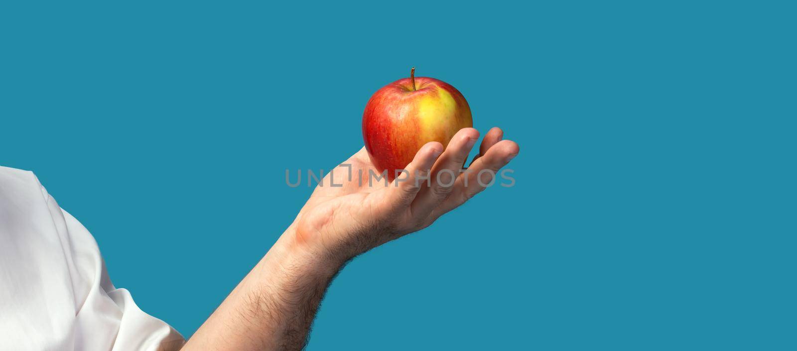 Healthy lifestyle and apple diet. Male hand with red apple on blue background