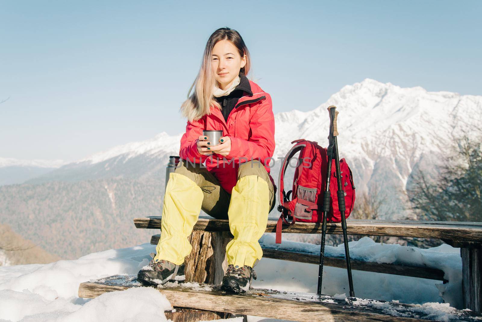 Hiker young woman drinking tea on background of mountains in winter.
