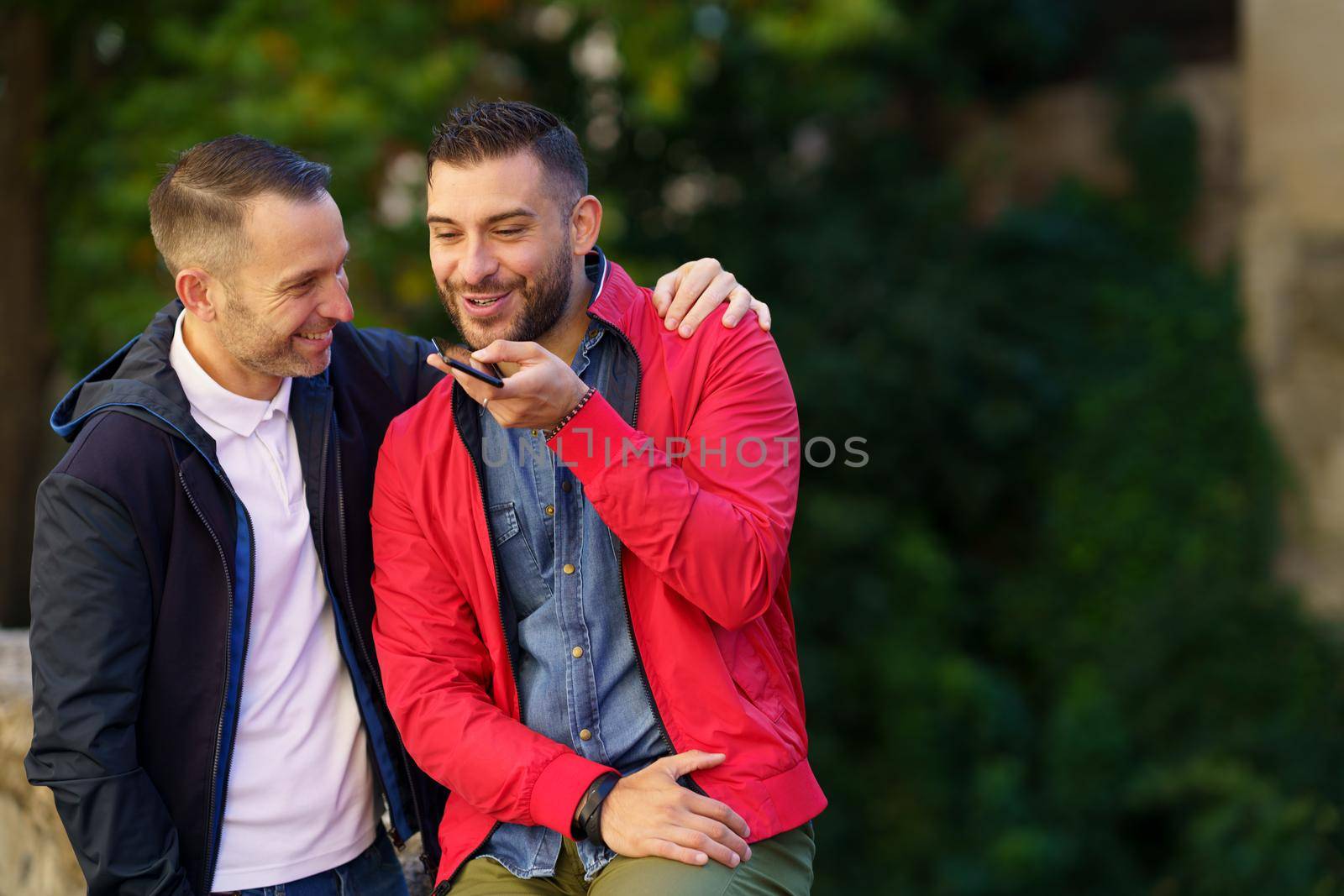 Gay couple recording a voice note together on their smartphone. Homosexual relationship concept.