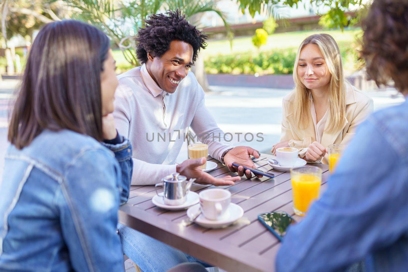 Multi-ethnic group of students having a drink on the terrace of a street bar. by javiindy