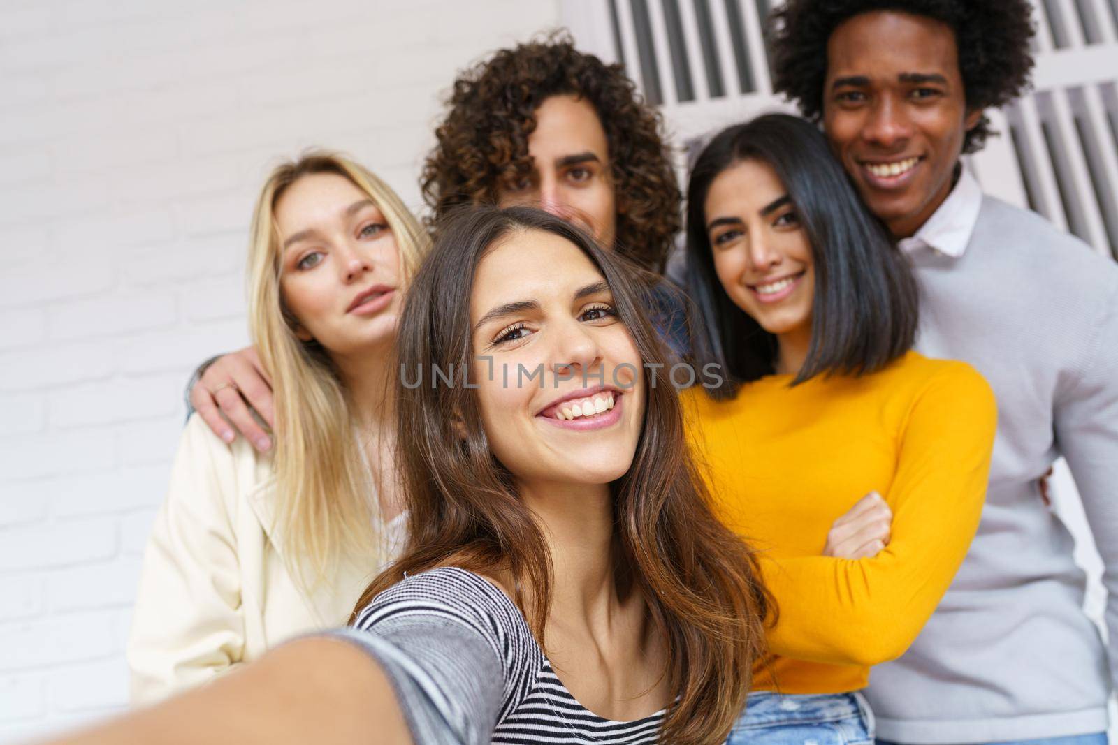 Multi-ethnic group of friends taking a selfie together while having fun in the street. Caucasian girl in the foreground.