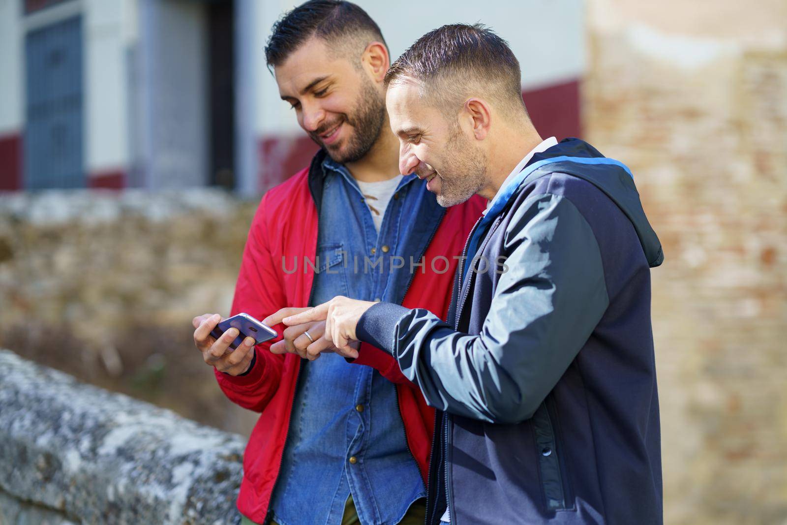 Gay couple looking at their smartphone outdoors by javiindy