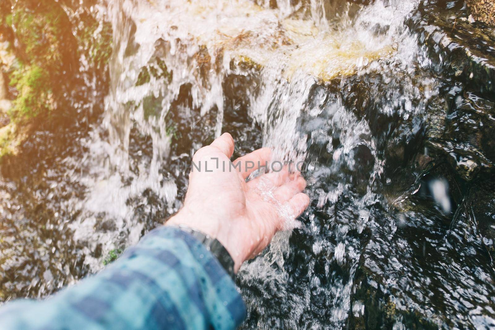 Male hand with water splash of mountain river outdoor.