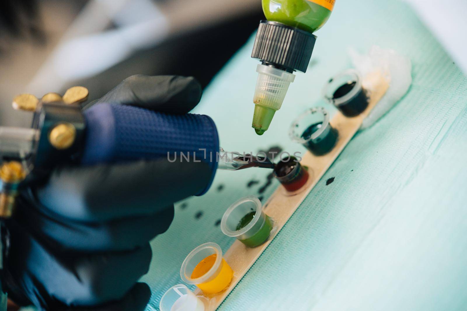 Female tattooist loading the tattoo machine with ink by mixing different colours. Tattoo concept.