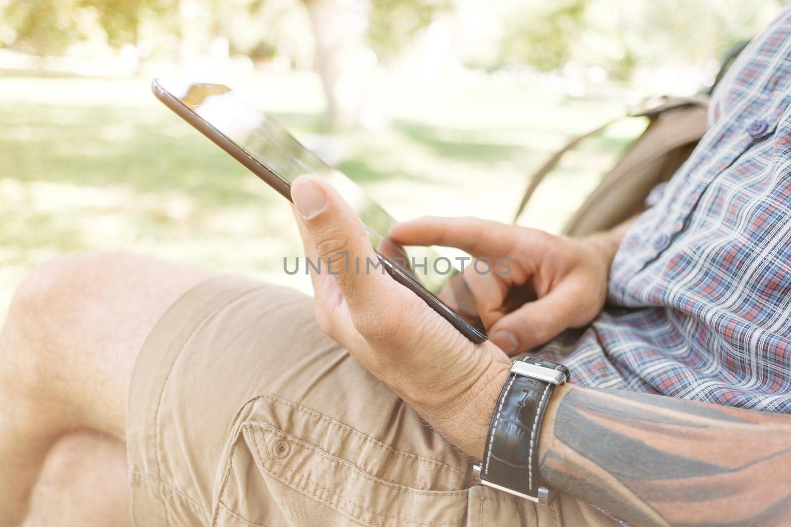 Young man using digital tablet in summer park, close-up of hands.