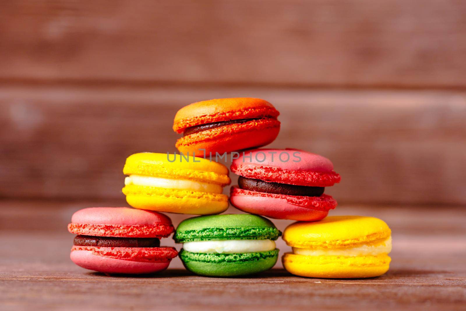 Stack of colorful macarons cookies on a wooden background.