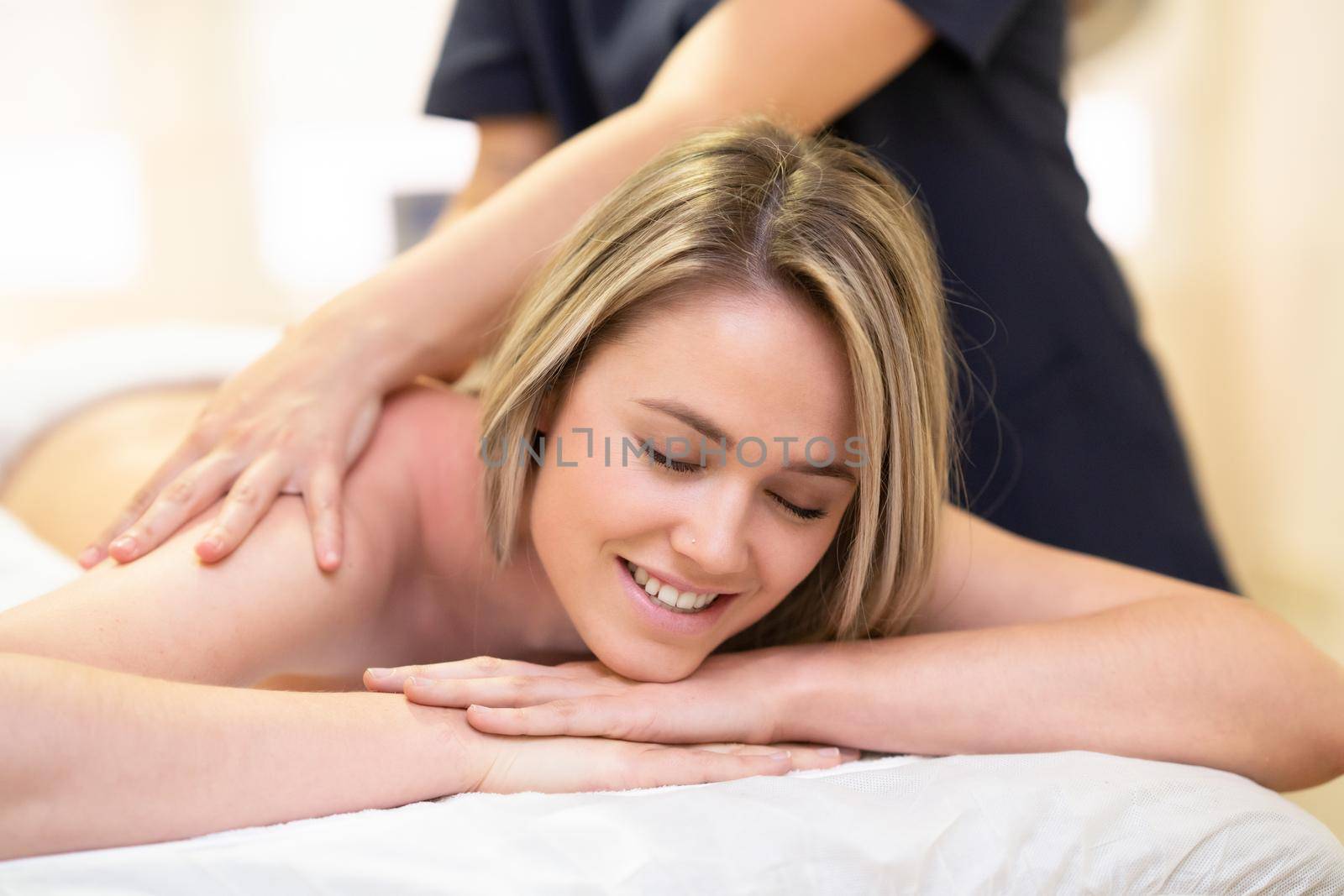 Young woman lying on a stretcher receiving a back massage in a physiotherapy center.