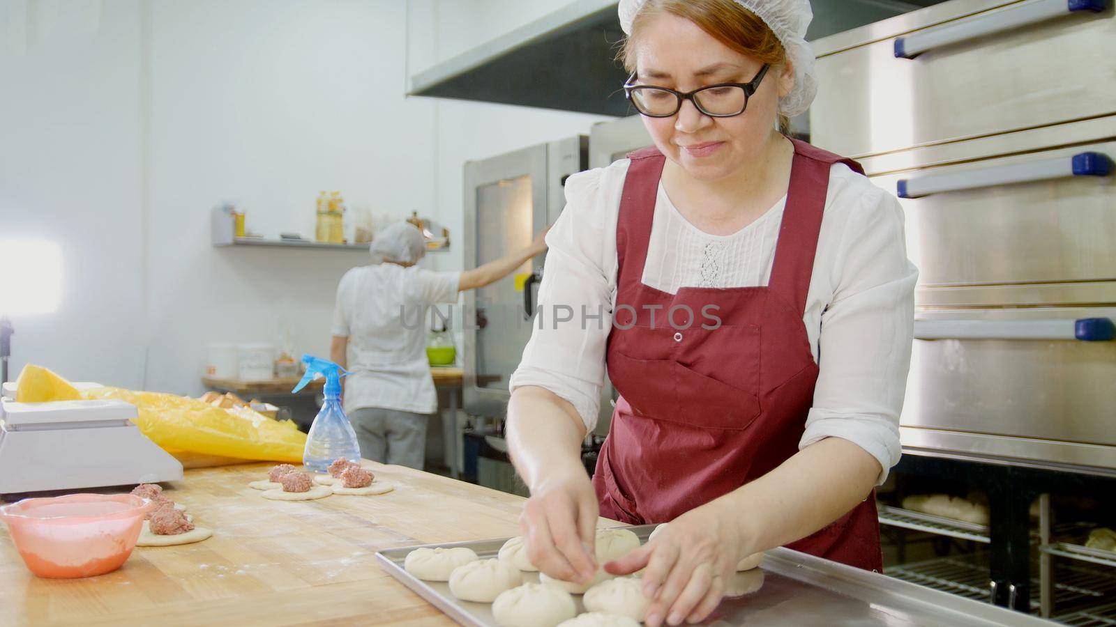 Woman in glasses and apron bakes cakes in the bakery, close-up