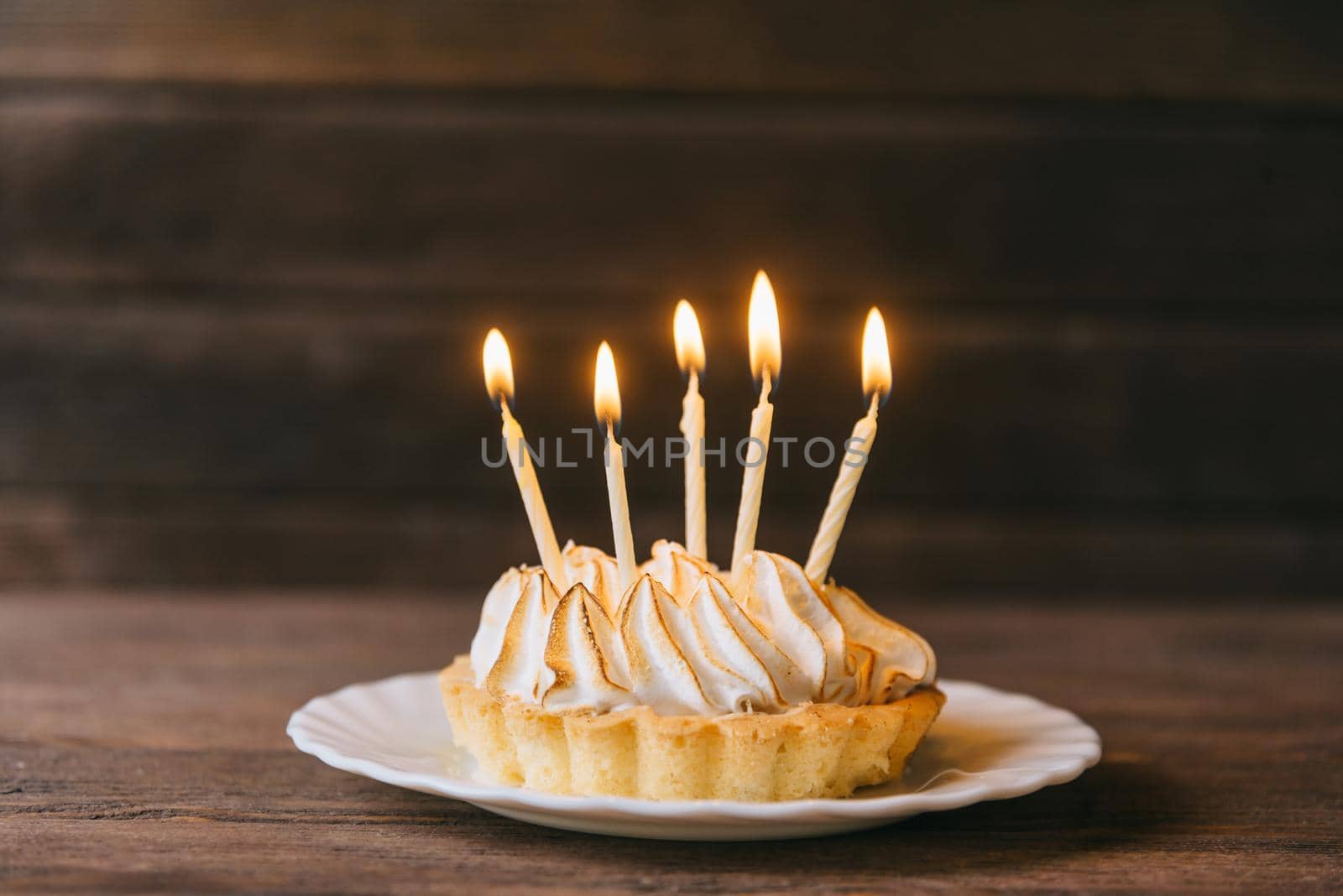 Birthday cupcake with five candles on a plate on wooden background.