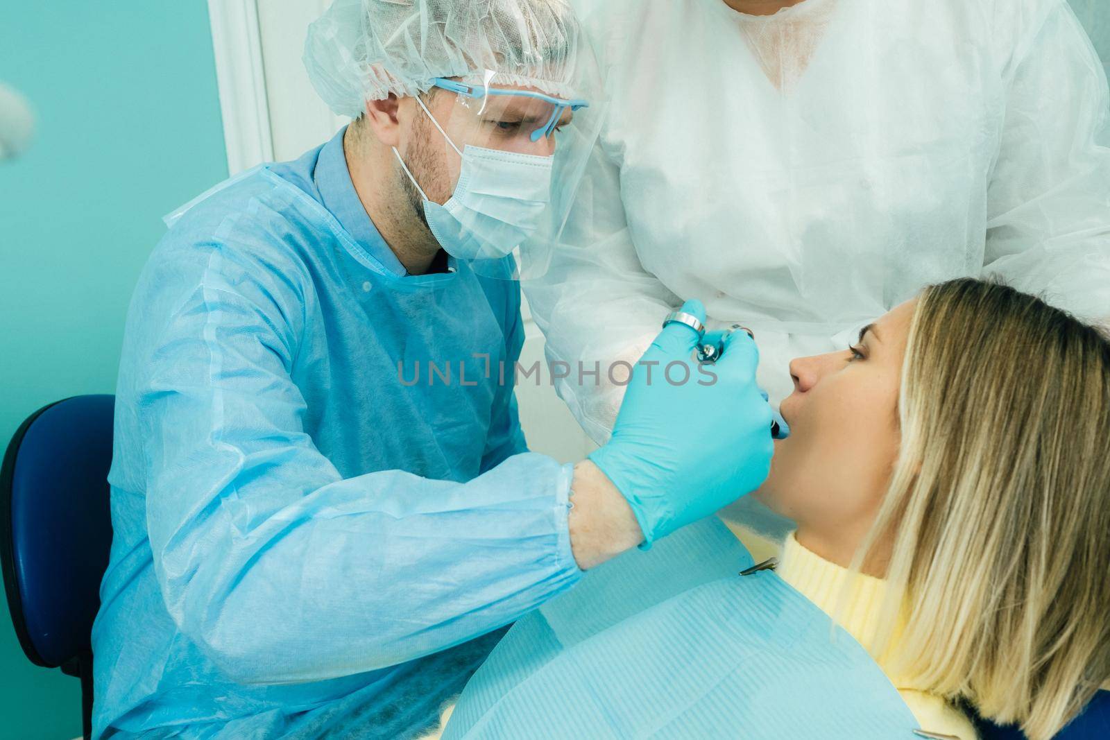 A male dentist with dental tools drills the teeth of a patient with an assistant. The concept of medicine, dentistry and healthcare by Lobachad