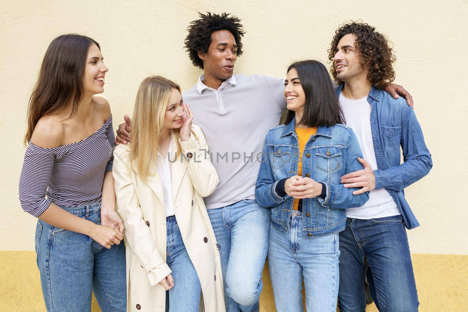 Multi-ethnic group of friends posing while having fun and laughing together against a yellow urban wall.