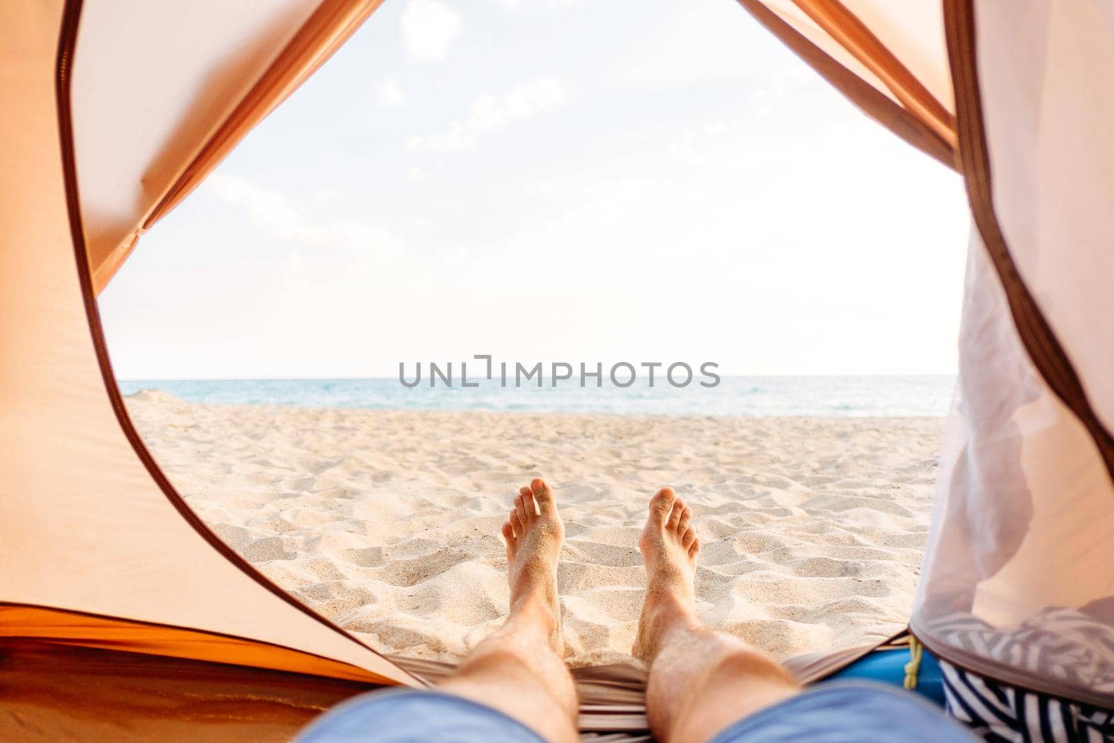 Young man resting in a tent on sand beach near the sea, point of view.