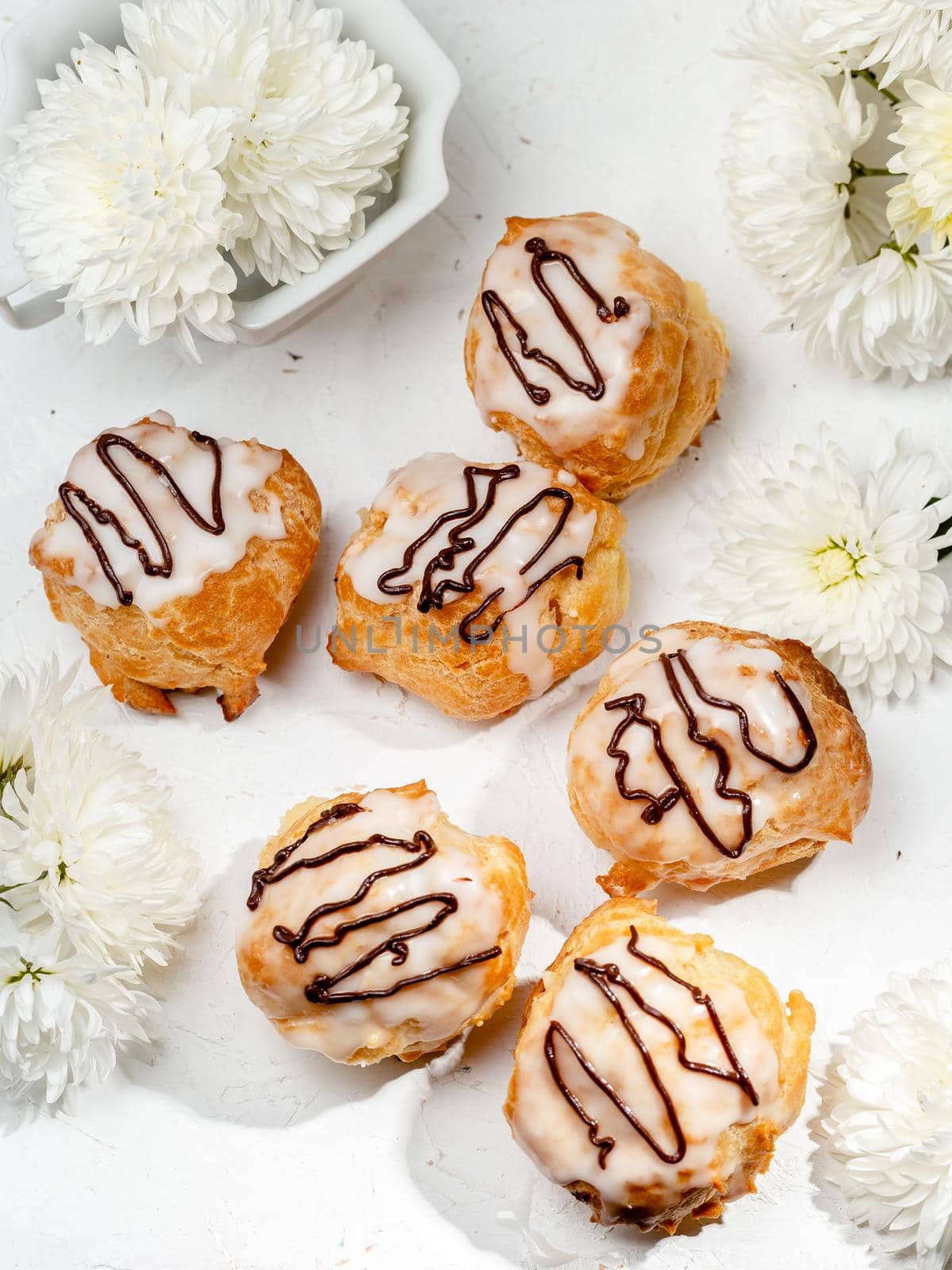Closeup view of delicious fresh profiteroles filled with custard on white table. Homemade tasty eclairs. Concept of desserts, restaurant food.