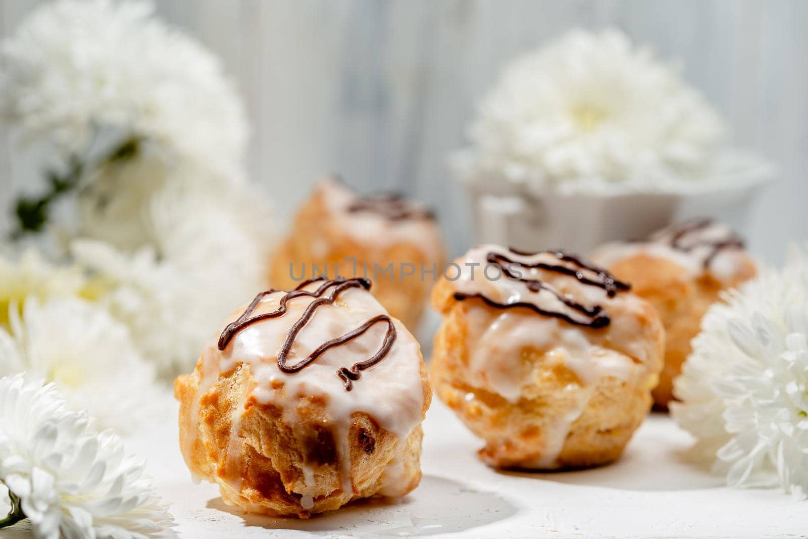 Closeup view of delicious fresh profiteroles filled with custard on white table. Homemade tasty eclairs. Concept of desserts, restaurant food.