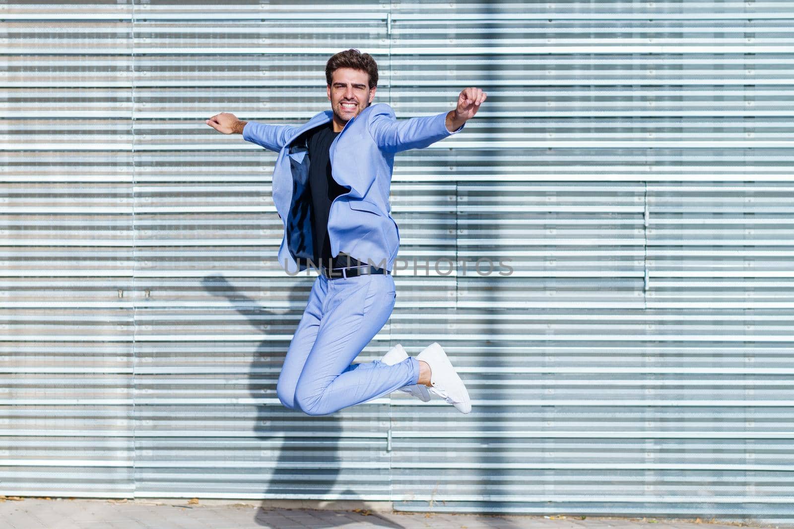 Young man wearing a suit jumping outdoors. Happy businessman in urban background.