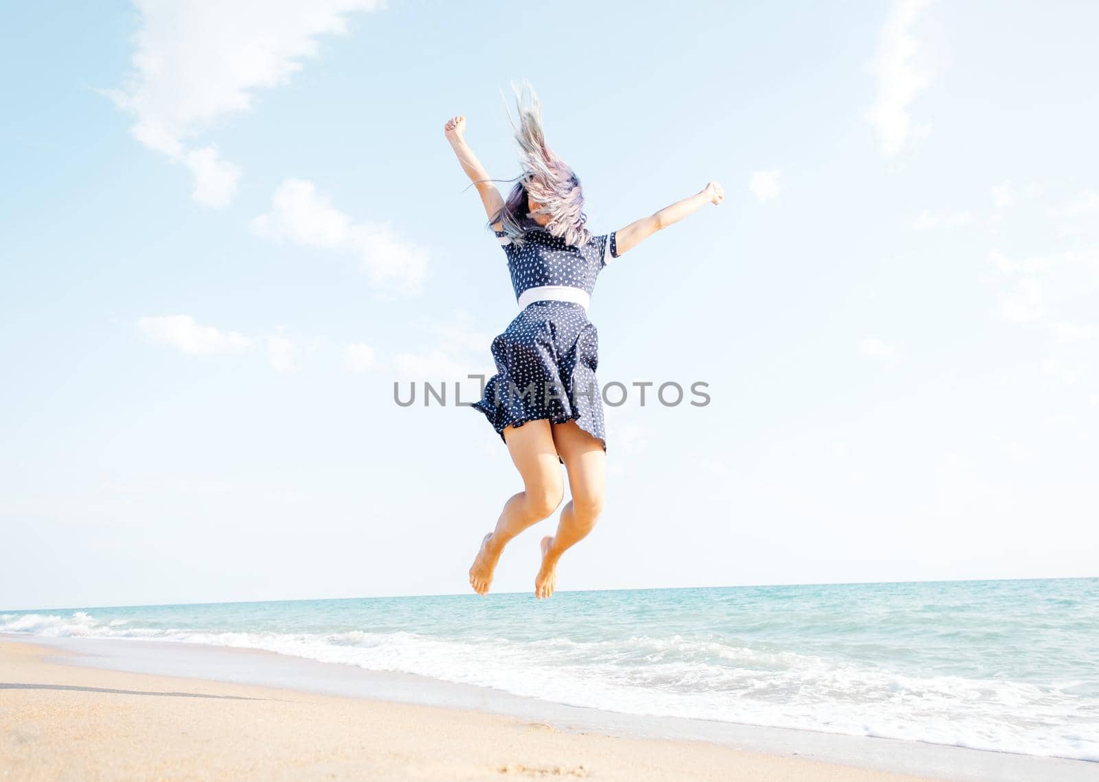 Happy young woman jumping on sand beach near the sea, summer vacations.