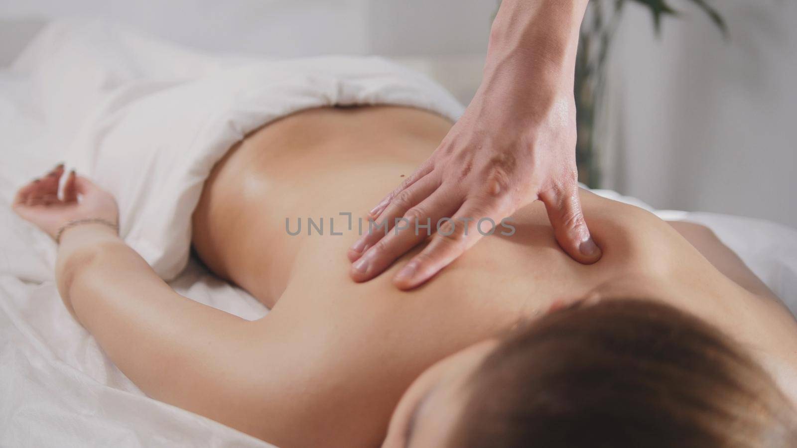 Blonde young woman model receiving relaxing massage in spa room, close up view