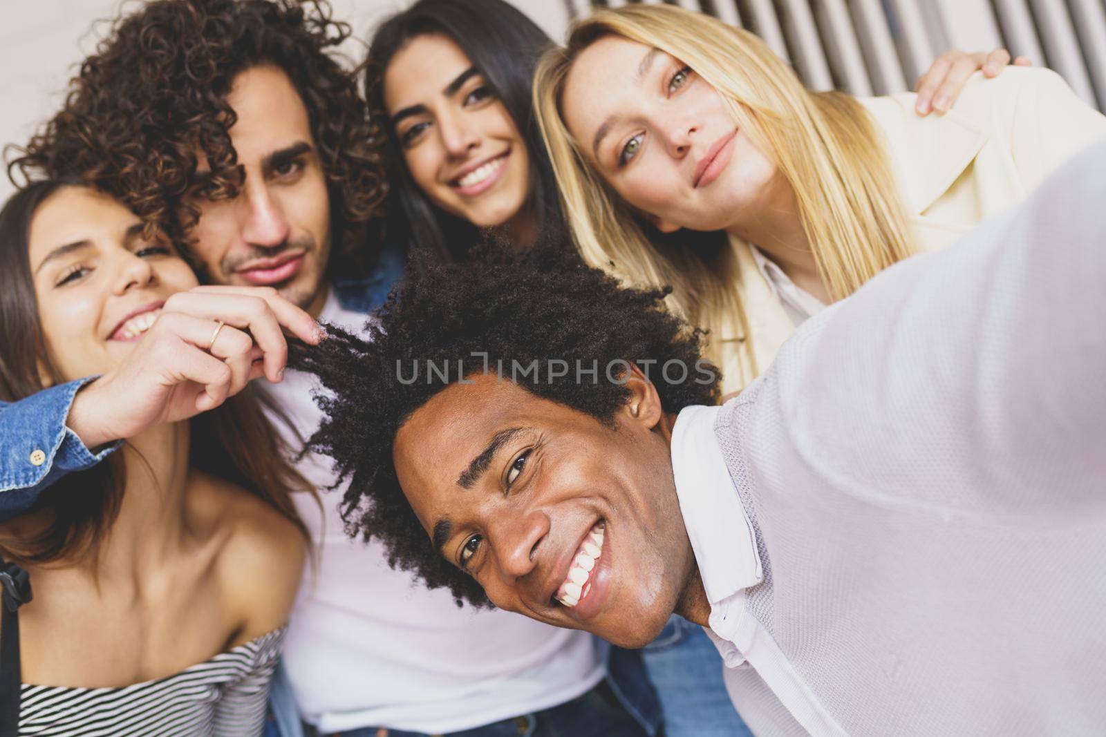 Multi-ethnic group of friends taking a selfie together while having fun outdoors. by javiindy