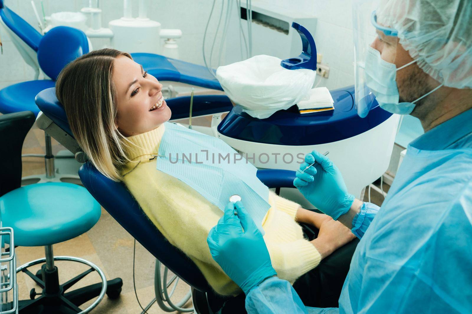 a dentist wearing a protective mask sits nearby and holds instruments in his hands before treating a patient in the dental office.