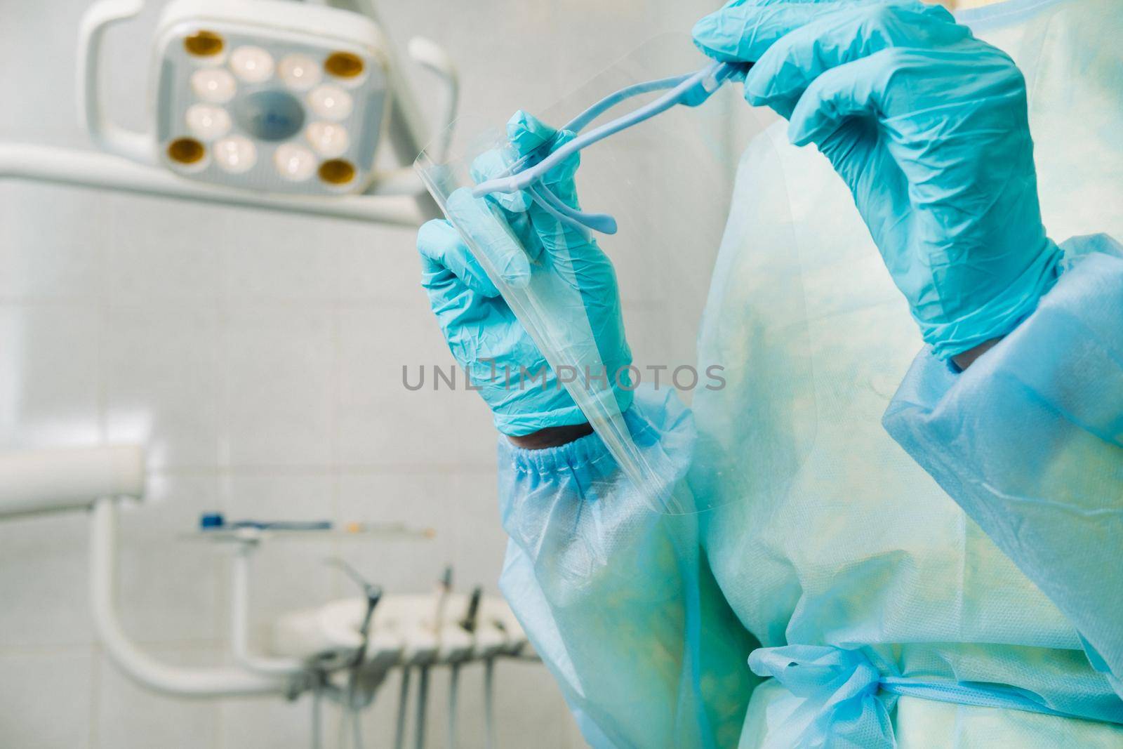 close up of a dentist's hands holding a protective plastic screen in his office by Lobachad