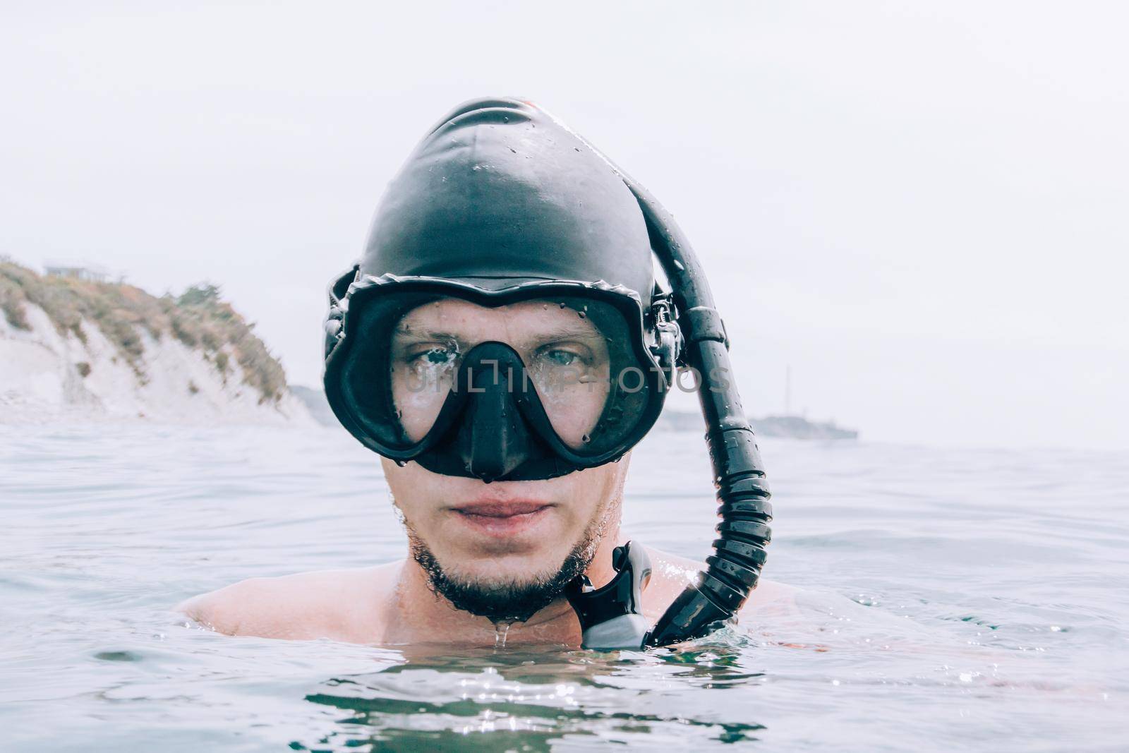 Portrait of young man freediver in mask and with snorkel above sea surface.