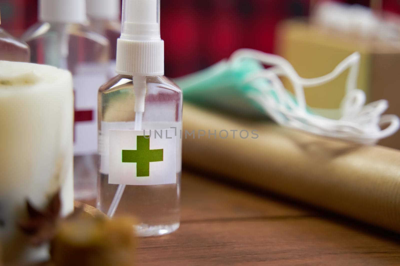 Alcohol antiseptic with the green cross logo on wooden background. Sanitizer, medical masks and roll of paper on table. Concept of hand hygiene and prevention from viruses and bacteria.