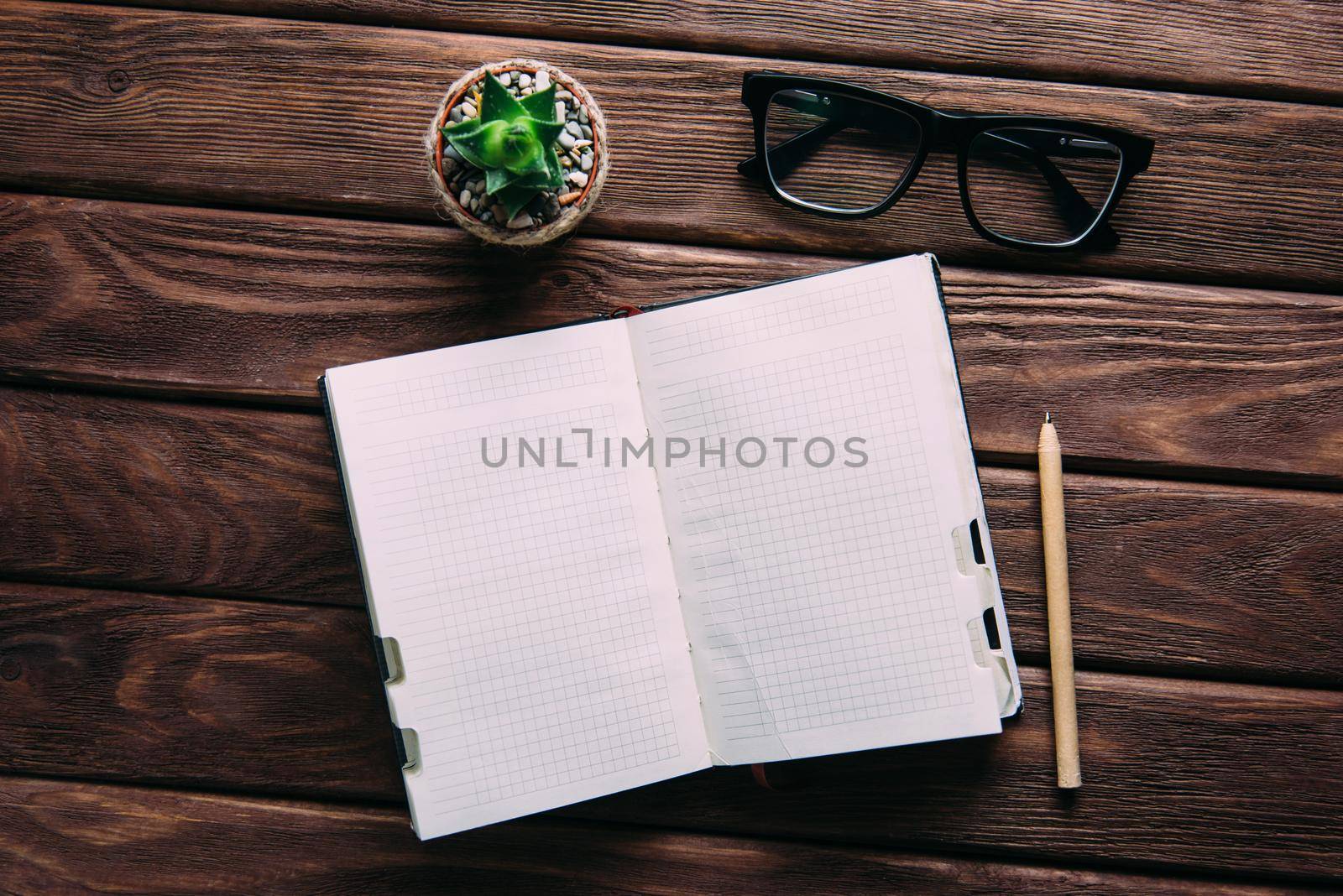Notebook with pen, glasses and small plant succulent on a wooden table, top view. Creative business workspace.