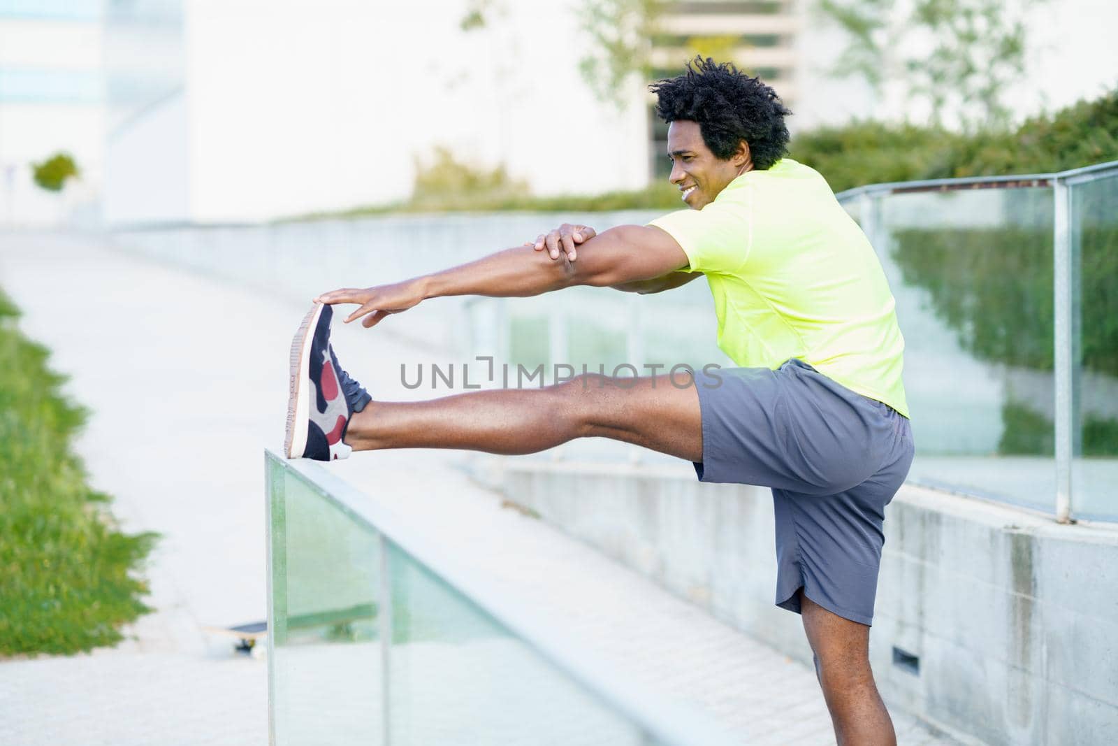 Black man with afro hair doing stretching after running outdoors. Young male exercising in urban background.