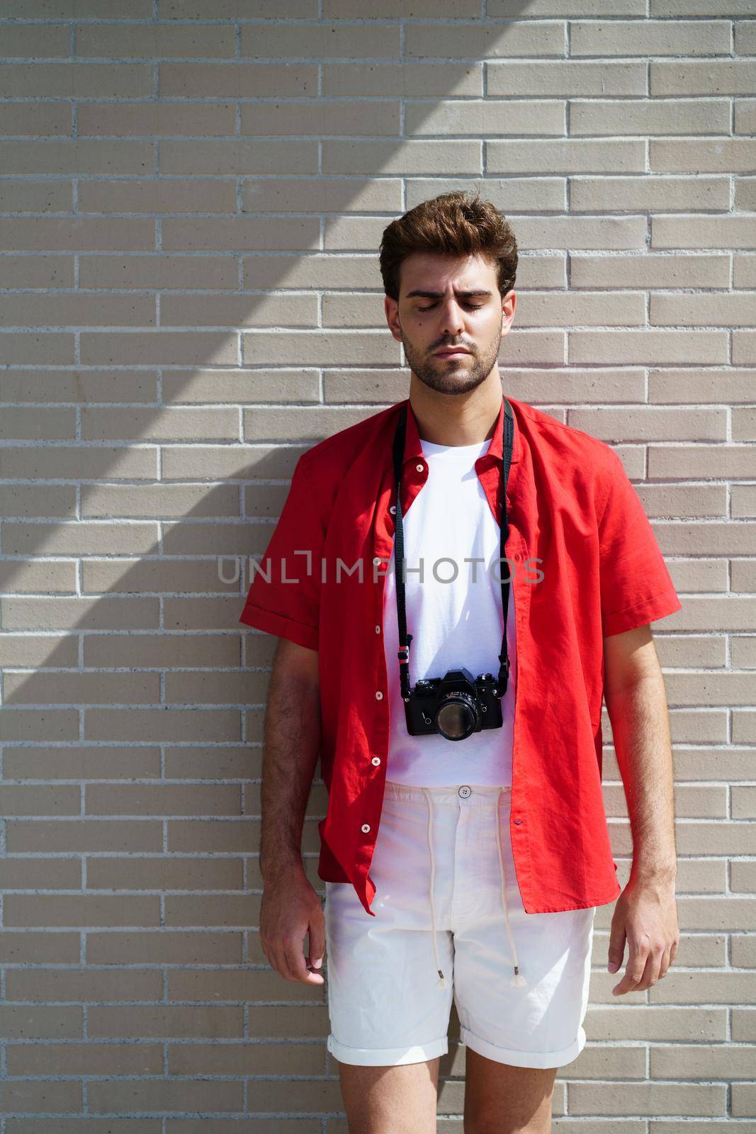 Millennial man traveling with a SLR camera outdoors. Male with eyes closed.