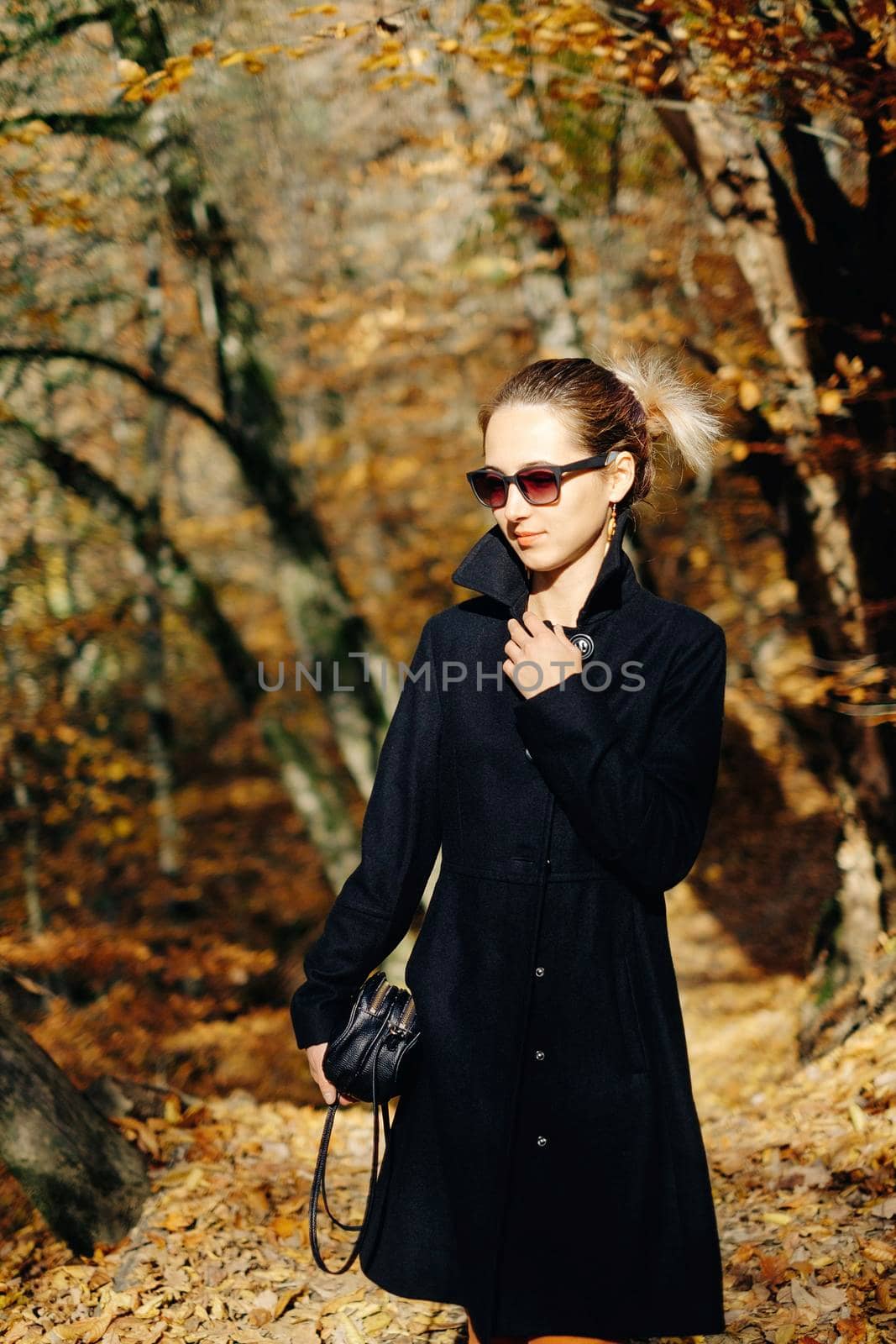 Fashionable young woman wearing in coat and sunglasses walking in autumn park.